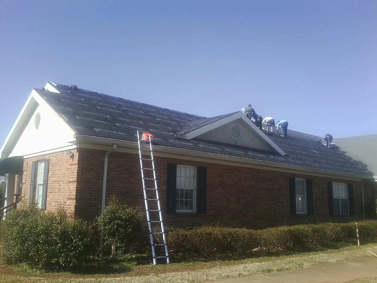 Crew tearing shingles off a brick ranch roof with a ladder set — Emergency Roof Repair work by our crew in Shrewsbury