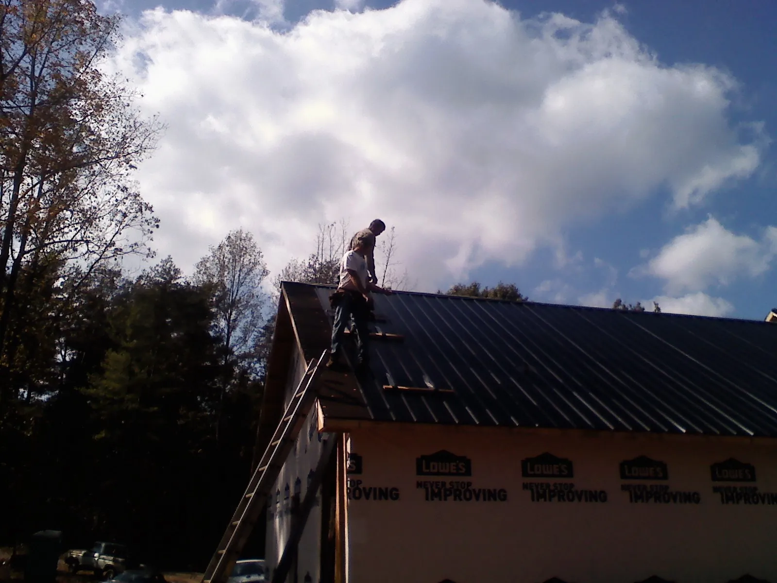 Roofer fastening dark metal panels high against a cloudy sky, from a Roof Inspection job in Shrewsbury
